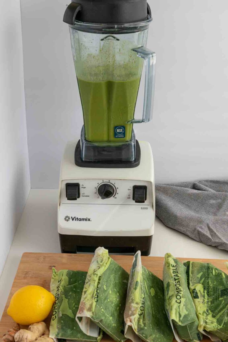 Green juice lined up in bags, with green smoothie in a blender in the background.